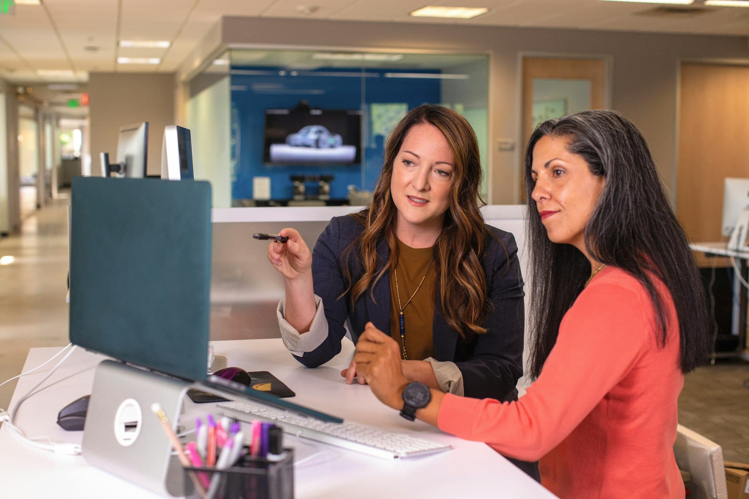 Two women at a desk, one pointing something out on the screen